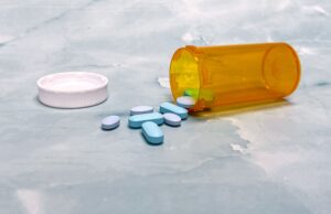 Medicaid Drug Prices May Fall. Patients Still Do Not Know Which Medicines Will Change Scattered blue pills and an orange prescription bottle on a light surface.