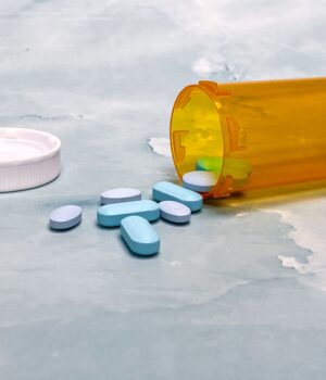 Scattered blue pills and an orange prescription bottle on a light surface.