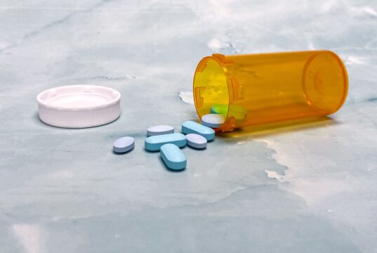 Medicaid Drug Prices May Fall. Patients Still Do Not Know Which Medicines Will Change Scattered blue pills and an orange prescription bottle on a light surface.