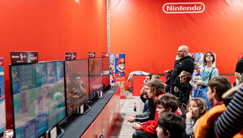 pexels-photo-19228377 A lively group enjoys gaming at a Nintendo event in Zagreb, featuring multiple screens and vibrant atmosphere.