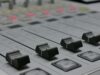 The Emergency Alert System Has a New Cybersecurity Rule. The Hard Part Is Knowing What It Touches. Detailed view of audio mixer sliders in a recording studio setting.