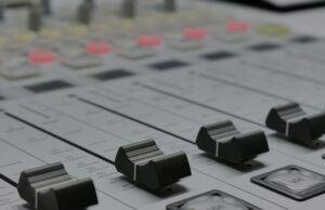 The Emergency Alert System Has a New Cybersecurity Rule. The Hard Part Is Knowing What It Touches. Detailed view of audio mixer sliders in a recording studio setting.
