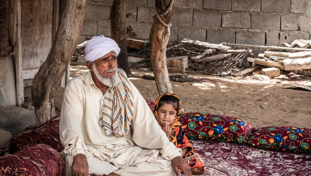 Elderly man and child sitting outdoors in traditional setting, Sistan and Baluchestan.