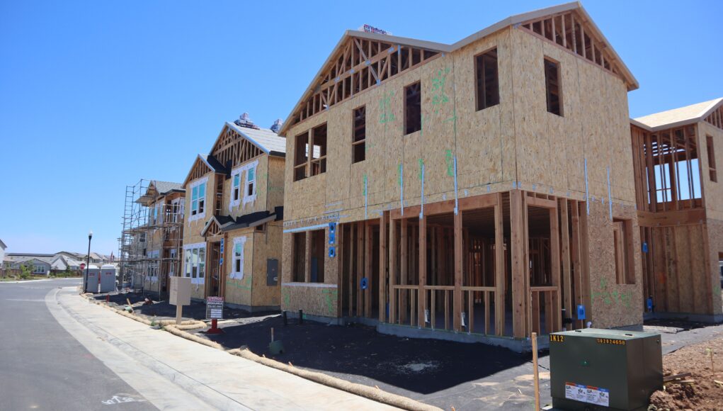 pexels-photo-38210398 Wooden frames of modern houses in construction in Elk Grove, California, under clear blue sky.