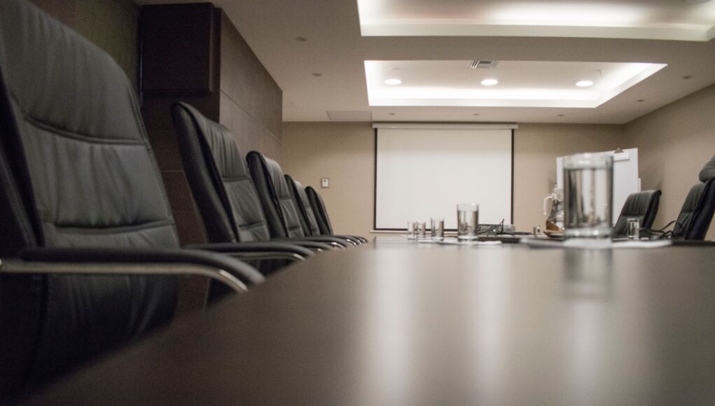 pexels-photo-3906592 Empty conference room with black chairs, projector, and glasses on table. Ideal for business meetings.