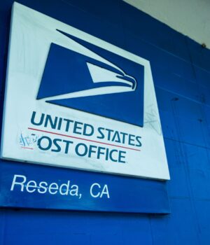 Close-up of the United States Post Office sign against a blue wall in Reseda, CA.