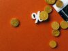 The Fed Raised Rates. Borrowers Will Pay Before Inflation Cools. Gold coins scattered with a stock market graph and a percentage symbol on an orange background.