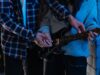 GTA VI Is Not Just Getting a Soundtrack. It Is Getting a Music Business Two young adults playing an electric guitar together in a cozy indoor setting, showcasing teamwork and learning.