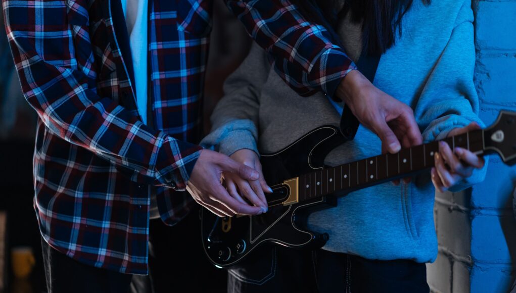 pexels-photo-7886316 Two young adults playing an electric guitar together in a cozy indoor setting, showcasing teamwork and learning.
