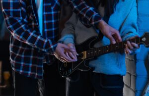 GTA VI Is Not Just Getting a Soundtrack. It Is Getting a Music Business Two young adults playing an electric guitar together in a cozy indoor setting, showcasing teamwork and learning.