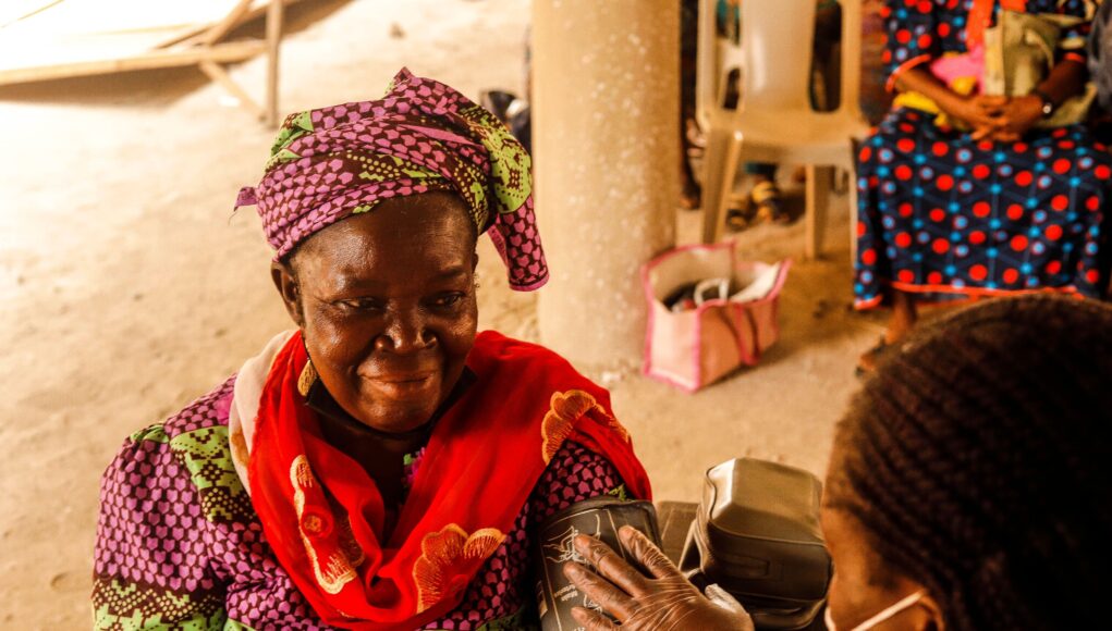 pexels-photo-8248293-1 A smiling woman in traditional clothing having her blood pressure measured by a healthcare worker.