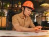 The Government Is Open. Federal Contractors Are Still Budgeting in the Dark. Young architect wearing helmet working on blueprint in modern office.