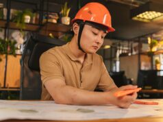 The Government Is Open. Federal Contractors Are Still Budgeting in the Dark. Young architect wearing helmet working on blueprint in modern office.