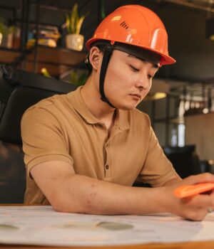 Young architect wearing helmet working on blueprint in modern office.