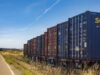 High Diesel Prices Are Giving Railroads Leverage. Shippers Still Have to Reach the Train. Colorful cargo containers on a freight train along a rural railway track under a clear blue sky.