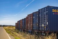 High Diesel Prices Are Giving Railroads Leverage. Shippers Still Have to Reach the Train. Colorful cargo containers on a freight train along a rural railway track under a clear blue sky.