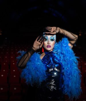 pexels-photo-13681747 A glamorous drag performer in a feather costume poses on a theater stage.