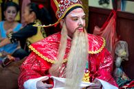 pexels-photo-14010703 A Chinese opera performer in a red costume prepares backstage with detailed makeup.