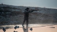 The Duck Stamp Bought the Wetland. Hunters Still Have to Find the Hunt. Man aiming rifle near pond with ducks during hunting session in misty dawn.