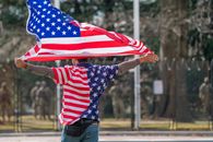 Washington’s Guard Deployment Is Becoming Permanent Before Its Legality Is Settled Man wearing American flag shirt and holding flag in Washington DC, symbolizing patriotism.