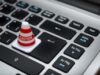 Chrome’s HTTPS Warning Is a Useful Security Upgrade. It Is Not a Trust Machine. Miniature caution cone on a computer keyboard symbolizing data security and control.