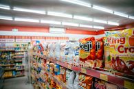 Tariff Refunds Are Reaching Corporate Ledgers. Consumers Are Still Waiting. Wide shot of vibrant snack aisle in a supermarket with various chip bags on display.