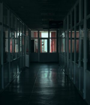 Gloomy indoor corridor with glass partitions and dim lighting in a modern office building.