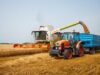 The Farm Rescue May Arrive After the Bills Are Due A modern tractor and harvester working in a wheat field during the summer harvest.