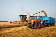 The Farm Rescue May Arrive After the Bills Are Due A modern tractor and harvester working in a wheat field during the summer harvest.