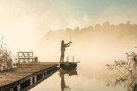 A Better Screen Can Find Bass. It Cannot Teach You the Water. A tranquil scene of a lone fisherman casting a line on a misty lake at sunrise.