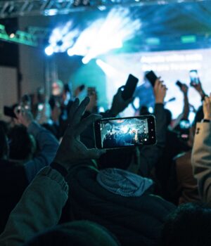 Lively crowd capturing concert moments on smartphones, vibrant lights create dynamic atmosphere.