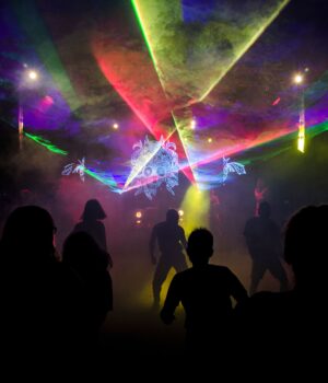 Silhouettes dance amid colorful laser lights in a vibrant nightclub setting.