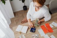 GDP Is Growing. Financial Flexibility Is Not Top view of a woman managing finances with a calculator, cash, and bills in a home setting.