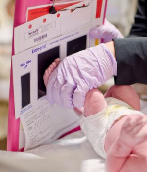 A newborn baby gets a footprint taken by a nurse in a hospital setting.