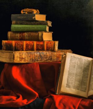 An artistic still life featuring a stack of vintage books and an olive lamp on rich red cloth.
