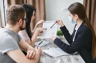 Open Enrollment Is Here. Families May Keep Insurance and Lose Their Children’s Hospital Three adults discuss a home insurance policy at a meeting table indoors.