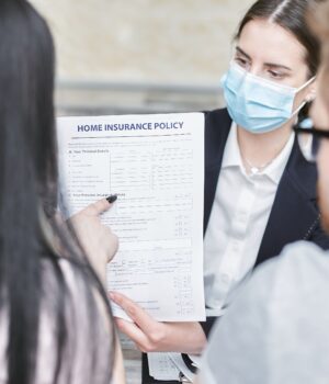 A professional woman explains a home insurance policy to clients during a meeting. Indoors setting.