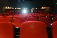 Theater Has Entered the Algorithmic Underworld A view of an empty cinema with rows of red seats facing the illuminated screen.