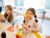 When SNAP Shrinks, the School Cafeteria Becomes the Next Safety Net Two smiling girls enjoying snacks during break time in a school classroom.
