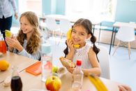 When SNAP Shrinks, the School Cafeteria Becomes the Next Safety Net Two smiling girls enjoying snacks during break time in a school classroom.