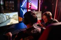 The Internet’s New Telethon Is a Game You Can Join Two gamers engaged in a heated video game session surrounded by neon lights and computer screens.